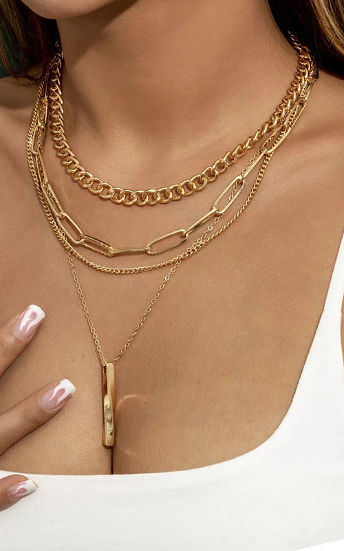 white model wearing a selection of gold layering chains, paperclip chains and heavy curb chain plus one with a pendant, model wearing white vest top and showing a few of her white nail varnish fingers within the image