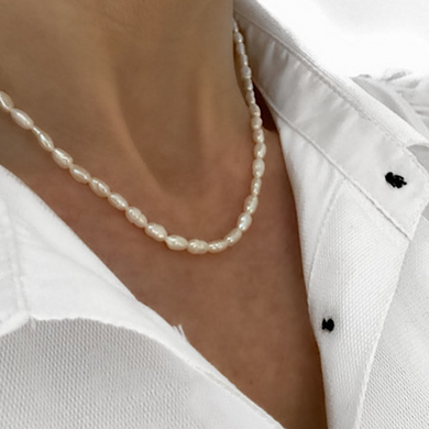 cultured pear necklace, single row with gold clasp worn by lady in white open buttoned shirt on white background