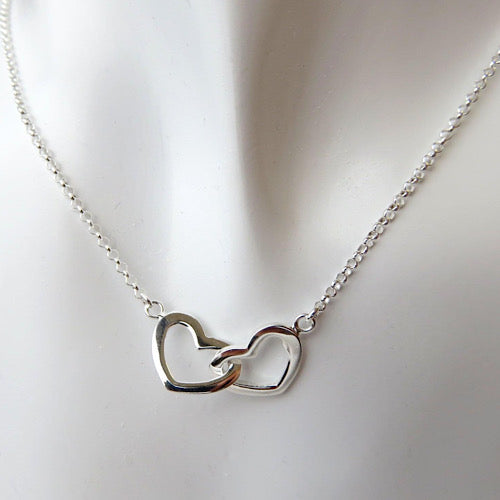 a duo of two 925 silver hearts interlinked with each other , plain hearts suspended on dainty silver chain on white background